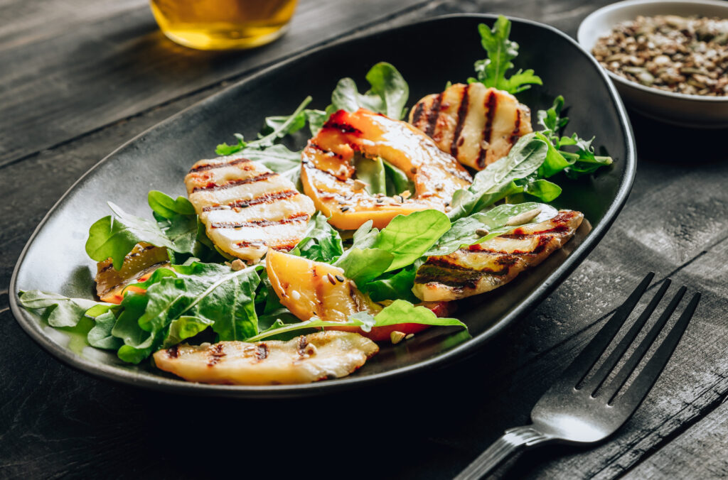 Grilled Halloumi Cheese Salad With Peach And Arugula On A Black Wooden Background. Healthy Food Concept.